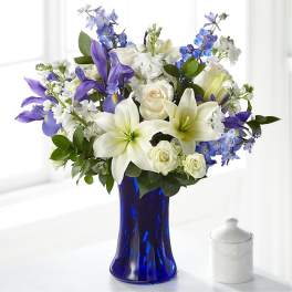 White lilies, roses, and blue-purple flowers in a cobalt vase