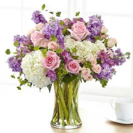 Pink roses and purple flowers arranged in a clear glass vase