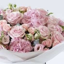 Bouquet of pale pink roses and ruffled pink flowers wrapped in white paper