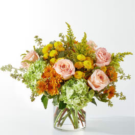 Bouquet of pink roses, green hydrangeas, and yellow-orange mums in a clear glass vase