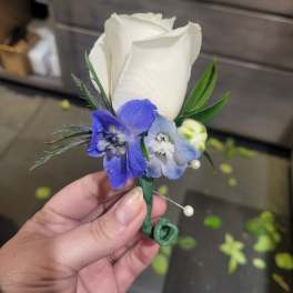 White rose boutonniere with blue flowers and green accents