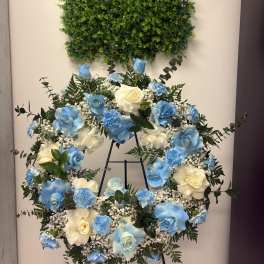 Blue and white rose wreath on a stand beneath a green foliage panel