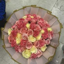 Round bouquet of pink and yellow roses with carnations in pale wrapping