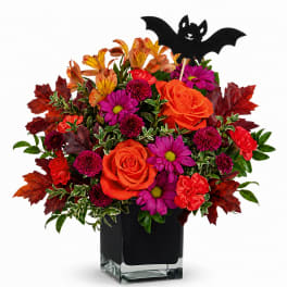 Orange and magenta flowers in a black vase with a bat pick