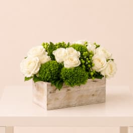 White roses and green pom flowers arranged in a wooden box