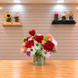 Bouquet of red roses, white daisies, and peach flowers in a glass vase