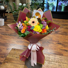 Mixed bouquet of roses, lilies, and a gerbera daisy wrapped in burgundy paper