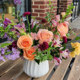 Mixed bouquet of peach, pink, and purple flowers in a white vase