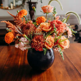 Orange and peach flowers arranged in a black vase on a wooden table
