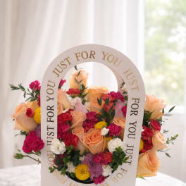 Mixed bouquet of peach roses, pink blooms, and yellow flowers in a white gift box