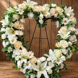 Heart-shaped floral wreath with white lilies, roses, and daisies on a stand