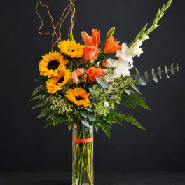 Tall bouquet of sunflowers, orange roses, and white gladiolus in a glass vase