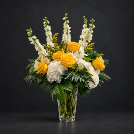 Yellow roses and white flowers arranged in a clear glass vase