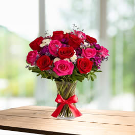 Bouquet of red and pink roses in a clear glass vase with a red ribbon