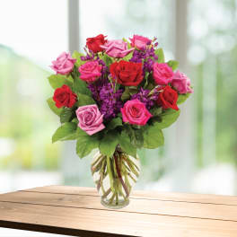 Bouquet of red, pink, and purple roses in a clear glass vase