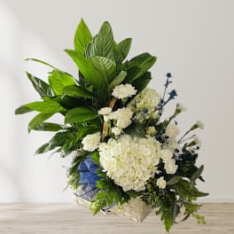 Large white floral arrangement with green foliage in a woven basket