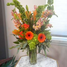 Tall mixed bouquet in a clear glass vase with orange and pink blooms