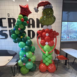 Two balloon sculptures, one Grinch-themed, standing indoors