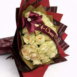 Bouquet of cream roses wrapped in burgundy and red paper with a satin bow