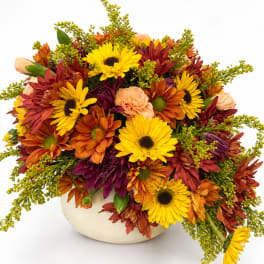 Mixed bouquet of yellow, orange, and burgundy flowers in a cream vase
