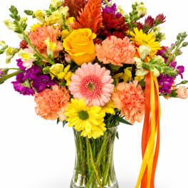 Mixed bouquet of bright flowers in a clear glass vase with ribbon