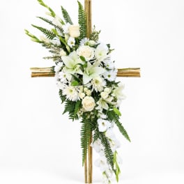 White floral cross arrangement with lilies, roses, and daisies on a bamboo cross