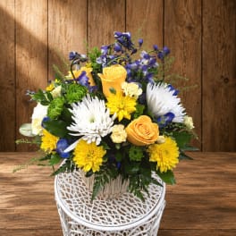 Yellow roses and white daisies in a white basket vase