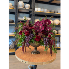 Deep red floral arrangement in a pedestal vase with hanging grape clusters