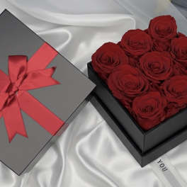 Box of red roses beside a gray gift box with a red ribbon