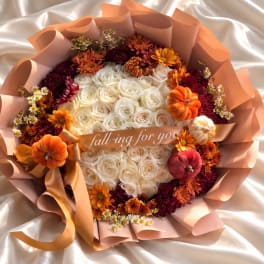 Round bouquet of white roses with orange and burgundy flowers and small pumpkins