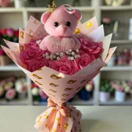 Pink teddy bear in a bouquet of pink roses with decorative wrapping