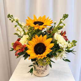 Sunflower arrangement in a decorative ceramic vase with white and red accent flowers
