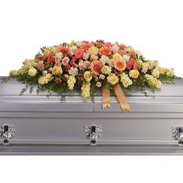 Pastel peach and yellow casket spray of roses and gerbera daisies on a silver casket