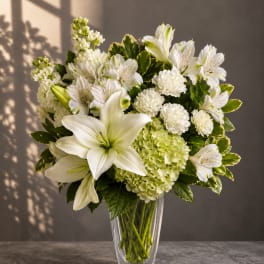 White lilies and mixed white flowers in a clear glass vase