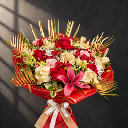 Bouquet of red and cream roses with a pink lily and gold palm fronds