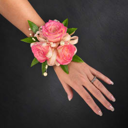 Pink rose wrist corsage with ribbon and pearl accents on a hand