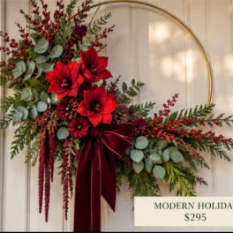 Holiday floral wreath with red blooms and a burgundy ribbon on a gold hoop