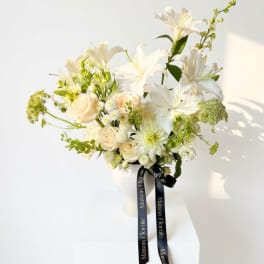 White lilies and cream roses in a white vase with a black ribbon