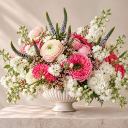 Pink and white mixed flower arrangement in a white pedestal vase