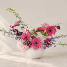 Pink gerbera daisies and mixed blooms in a white vase