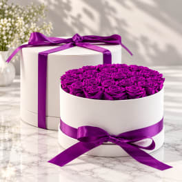 Two white round boxes filled with purple roses and tied with purple ribbon