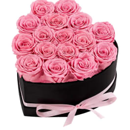 Pink roses arranged in a black heart-shaped box with a pink ribbon