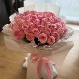 Bouquet of pink roses wrapped in white paper with a pink ribbon
