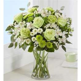 Green and white bouquet of roses, carnations, and daisies in a clear glass vase