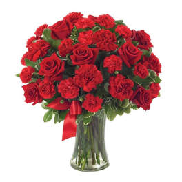 Red roses and carnations in a clear glass vase with a red ribbon