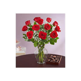 Red roses in a glass vase with a box of chocolates beside them