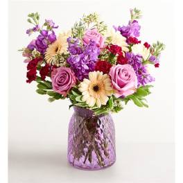Mixed bouquet of pink, purple, and cream flowers in a purple glass vase