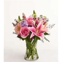 Pink roses, lilies, and daisies arranged in a clear glass vase