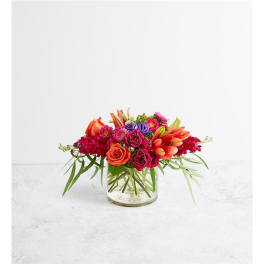 Low bouquet of orange, pink, and purple flowers in a clear glass vase