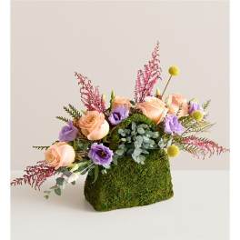 Peach roses and purple blooms in a moss-covered container
